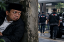 Ilustrasi dramatis Nusron Wahid yang digambarkan sedang duduk bersembunyi di balik tembok sambil mengamati situasi di sekitarnya. (Visual AI).