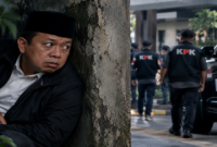 Ilustrasi dramatis Nusron Wahid yang digambarkan sedang duduk bersembunyi di balik tembok sambil mengamati situasi di sekitarnya. (Visual AI).