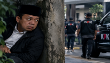 Ilustrasi dramatis Nusron Wahid yang digambarkan sedang duduk bersembunyi di balik tembok sambil mengamati situasi di sekitarnya. (Visual AI).